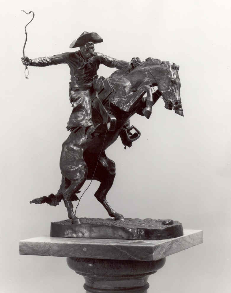black and white photograph of a statue of a cowboy riding a bucking horsee
