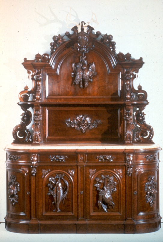 a large wood sideboard with a marble counter top, the wood is extravagantly decorated with carvings of fish, game, and vegetation in high relief