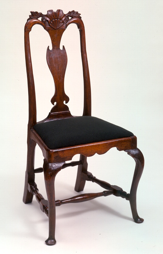 an armless wood chair with a shell decoration at the top and a blue seat cushion