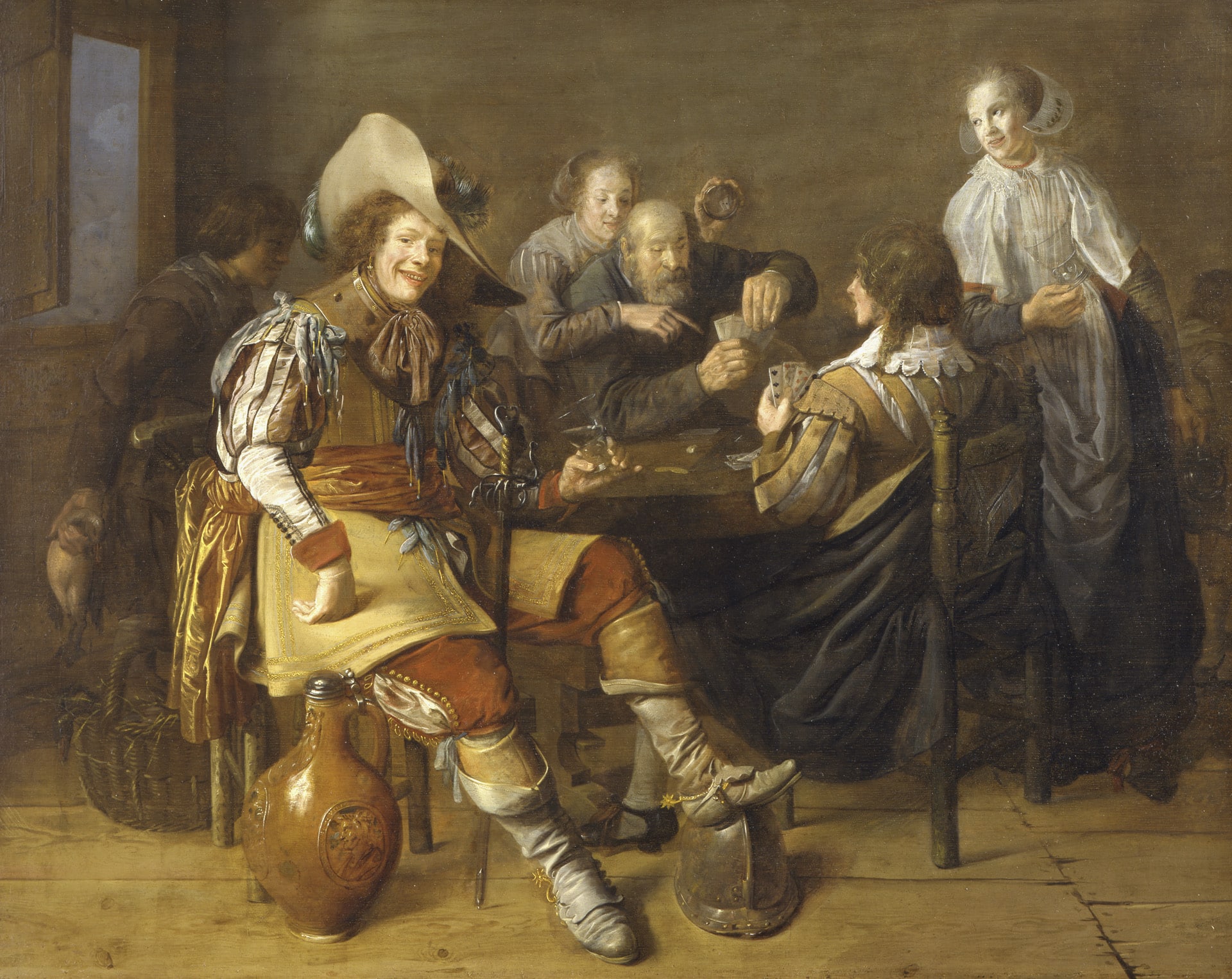 an interior of a tavern with men and women playing cards dressed in 17th century costume, one man looks out to the viewer with a smile
