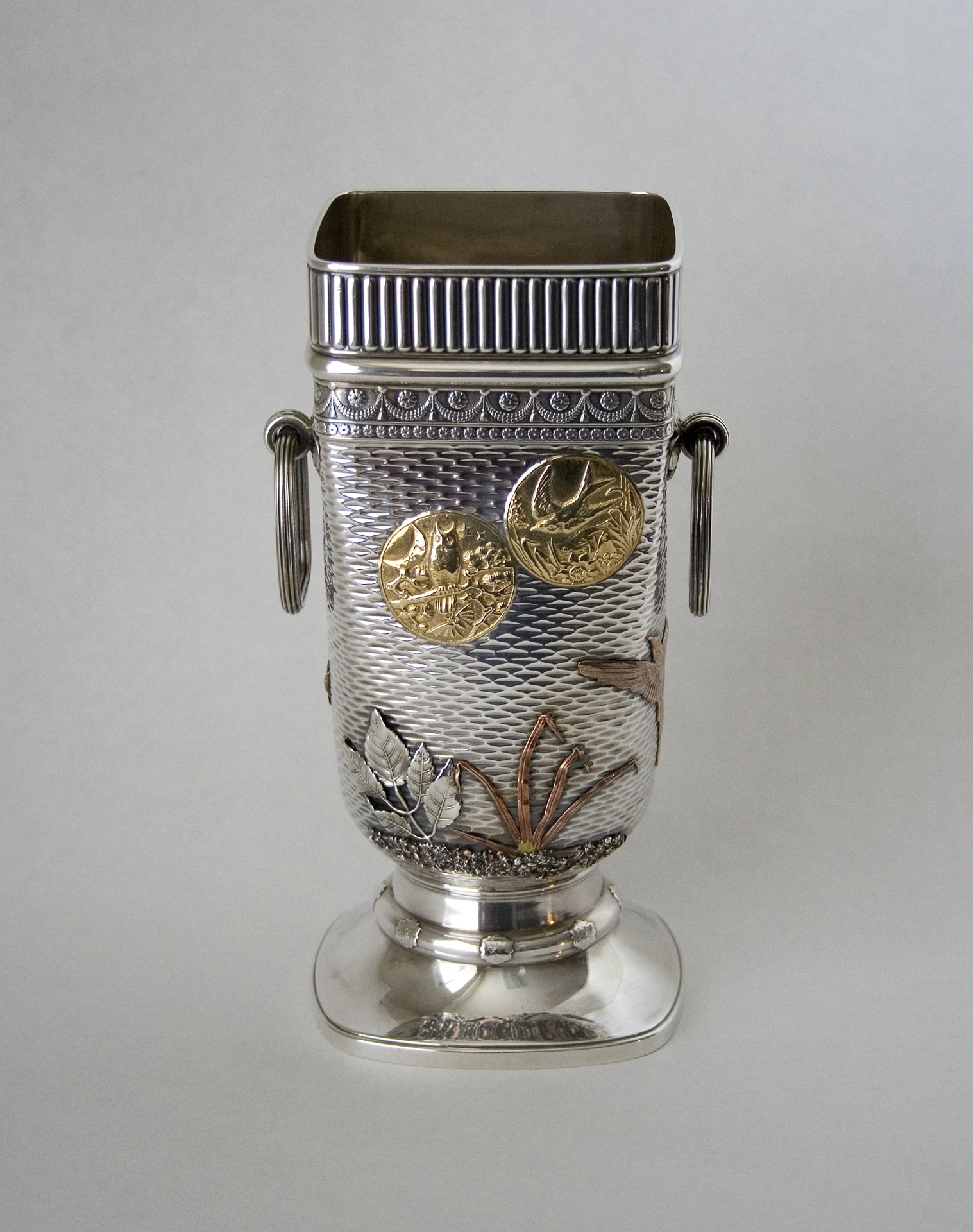 a silver vase with gold and copper decorative appliques