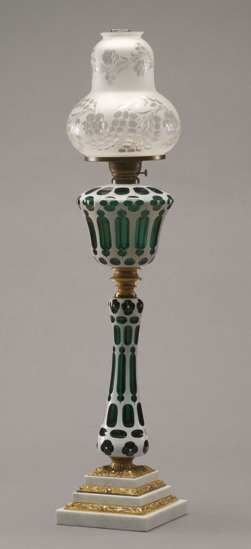 a tall glass lamp with a gold-stepped base and green glass decoration on the stem