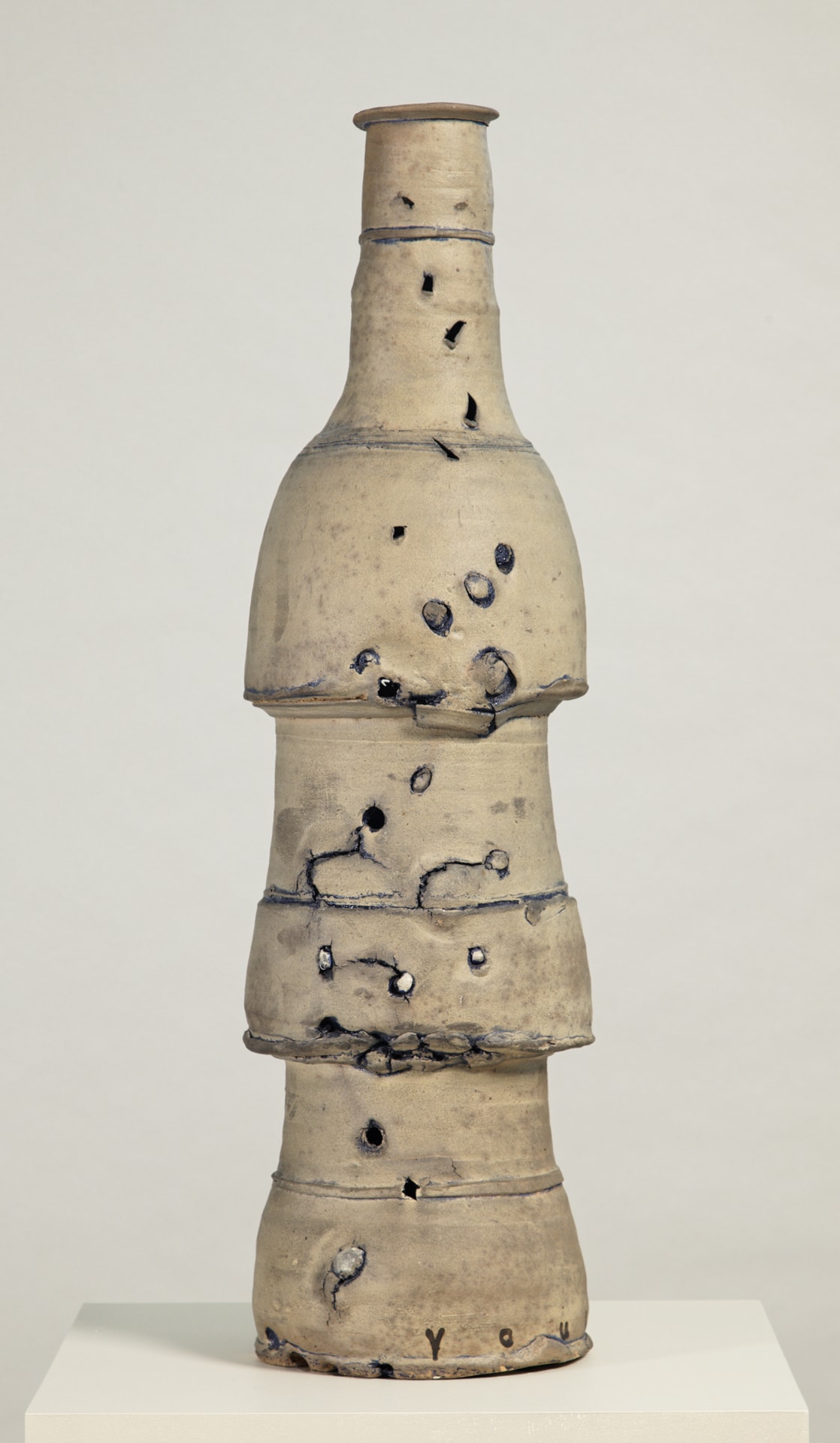 a tall ceramic vessel, colored beige, its surface is punctured