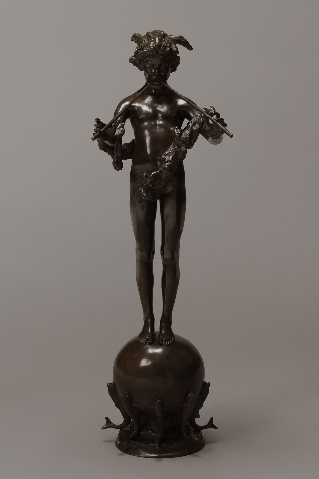 a bronze statue of a young nude boy playing a flute