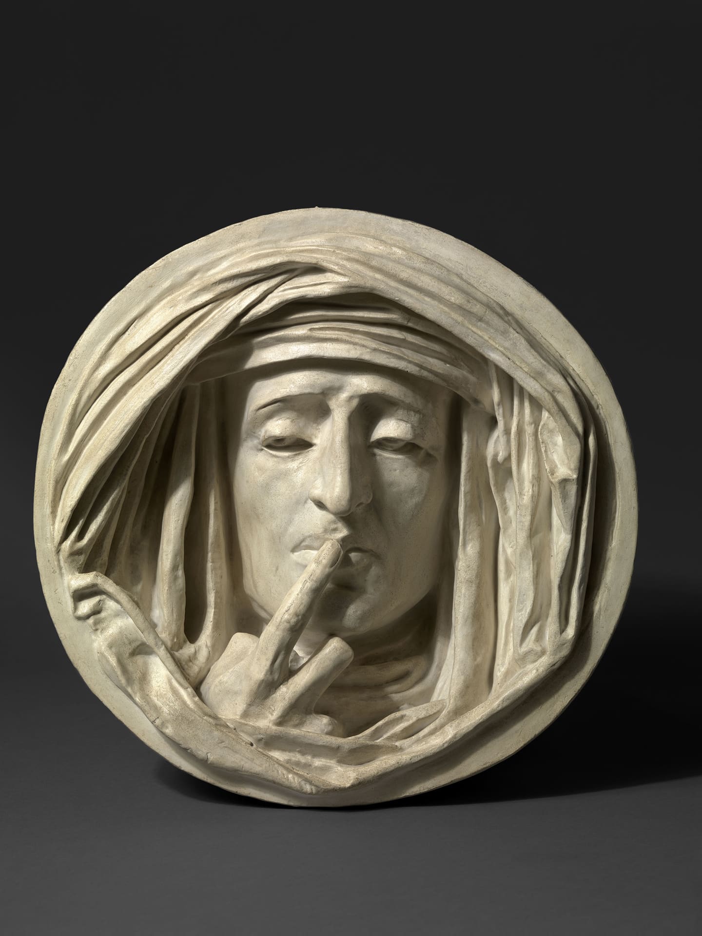 a sculpture of a woman's face holding her finger to her lips, in a circle