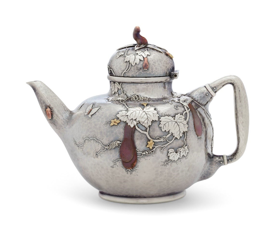 a silver teapot with vinous decoration in gold and copper