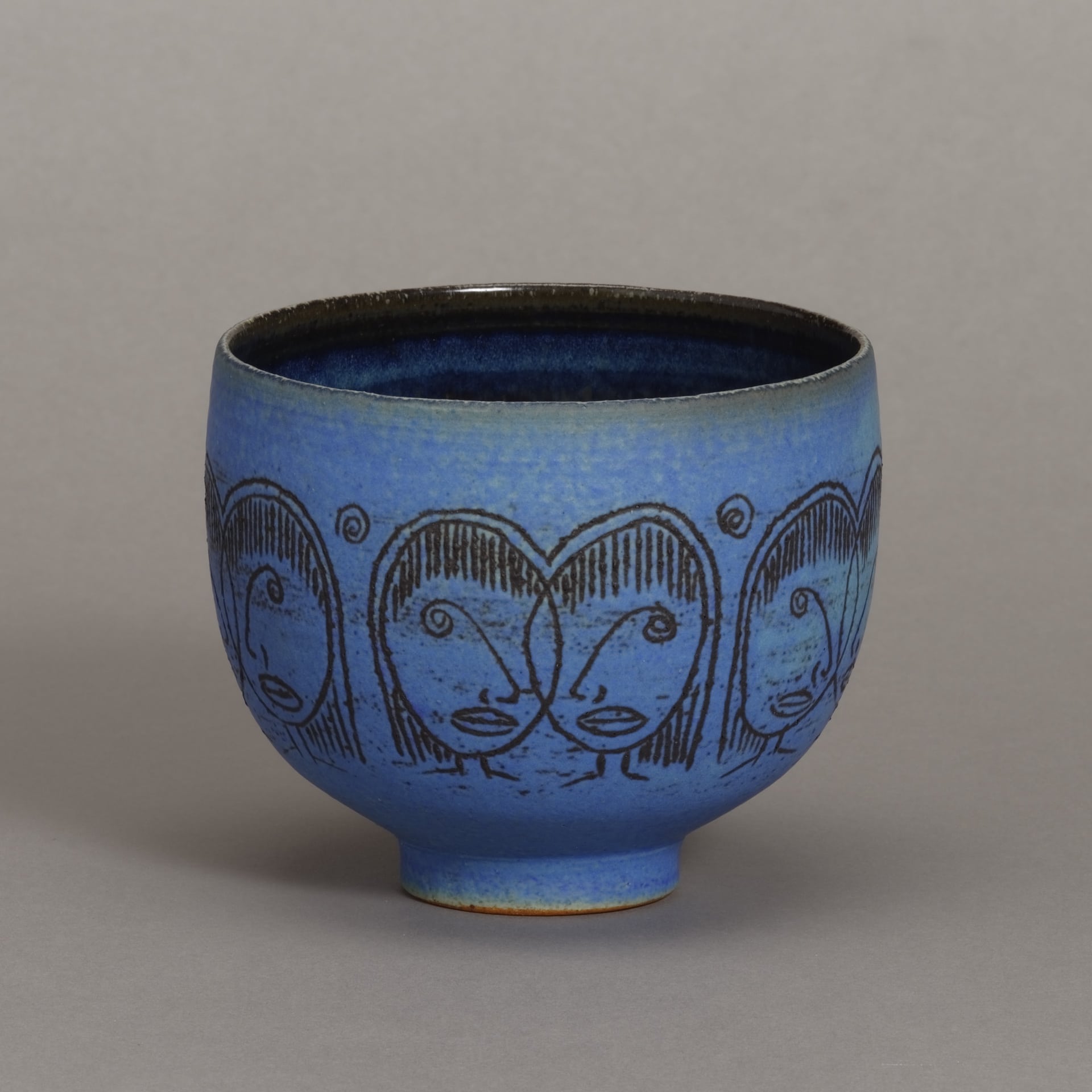 a footed blue bowl with faces etched around the middle