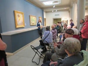 a group of older adults seated in a gallery looking at art