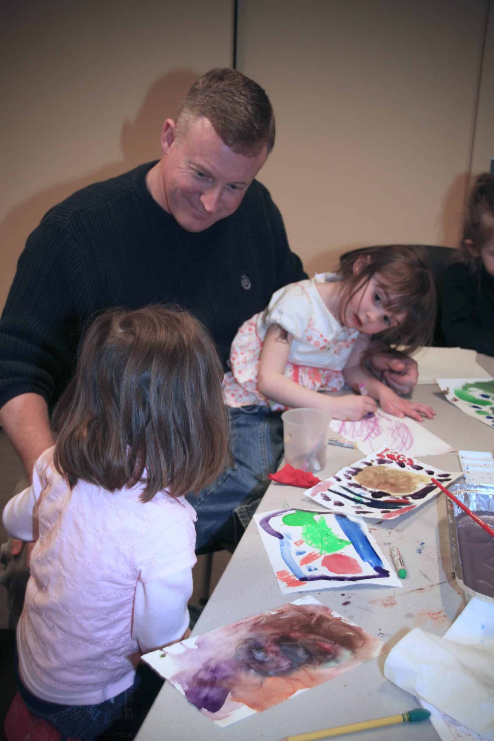 two young children are drawing at a table with their father