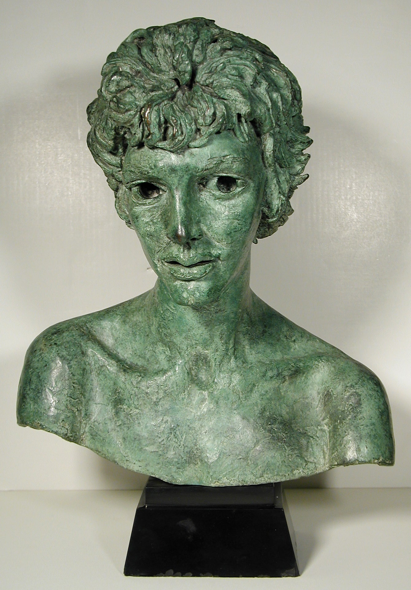 a bronze with green patina bust sculpture of a woman with short hair, visible collarbone and hollow eyes