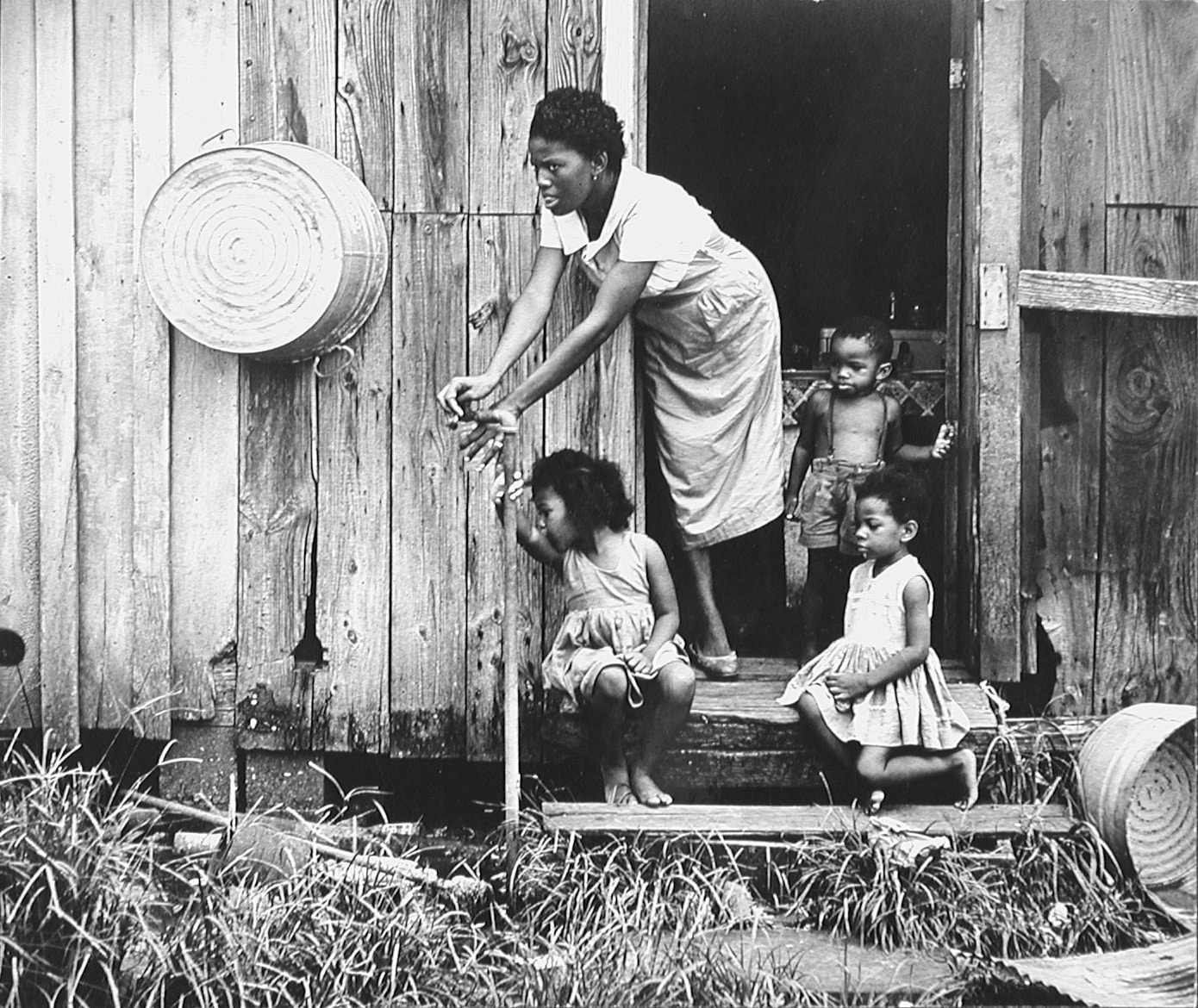 a black and white photograph of a mother and three children on the stoop of a wooden house