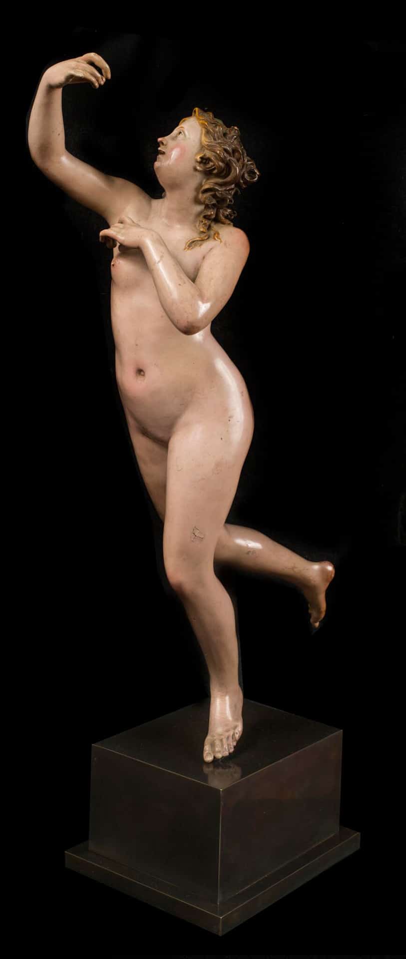 a painted sculpture of a woman running with one leg extended behind her, completely nude, arm raised as if holding something to her face